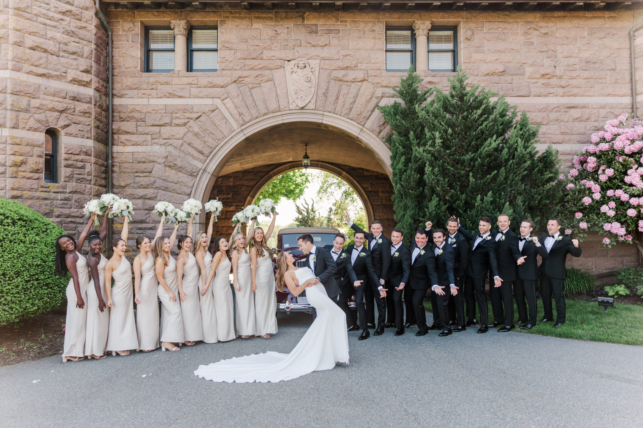 Bride and groom kiss in front of their cheering bridal party at the OceanCliff Hotel in Newport Rhode Island.