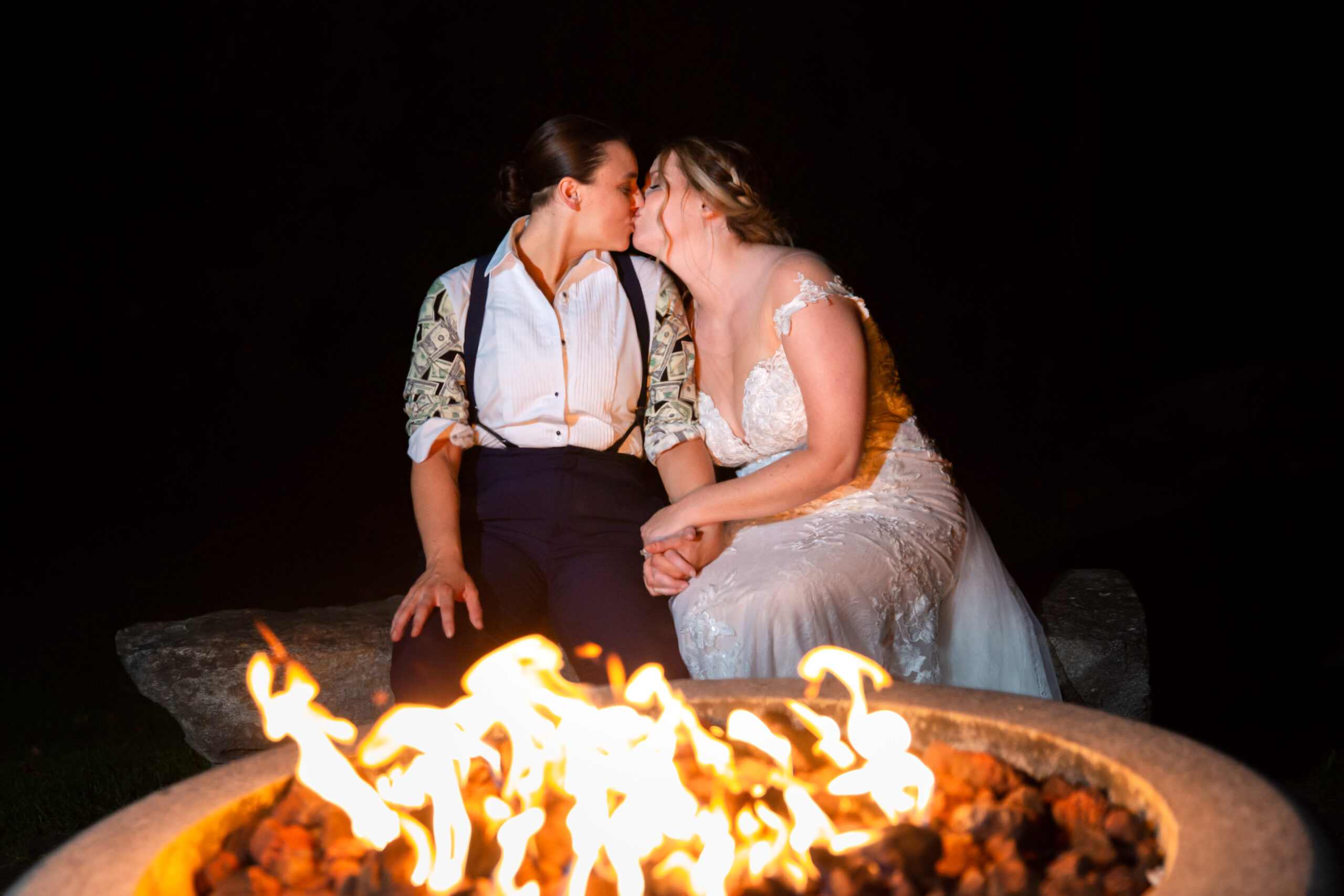Two brides kiss outside the Barn at the Outdoor fire pit at Zukas Hilltop Barn. 