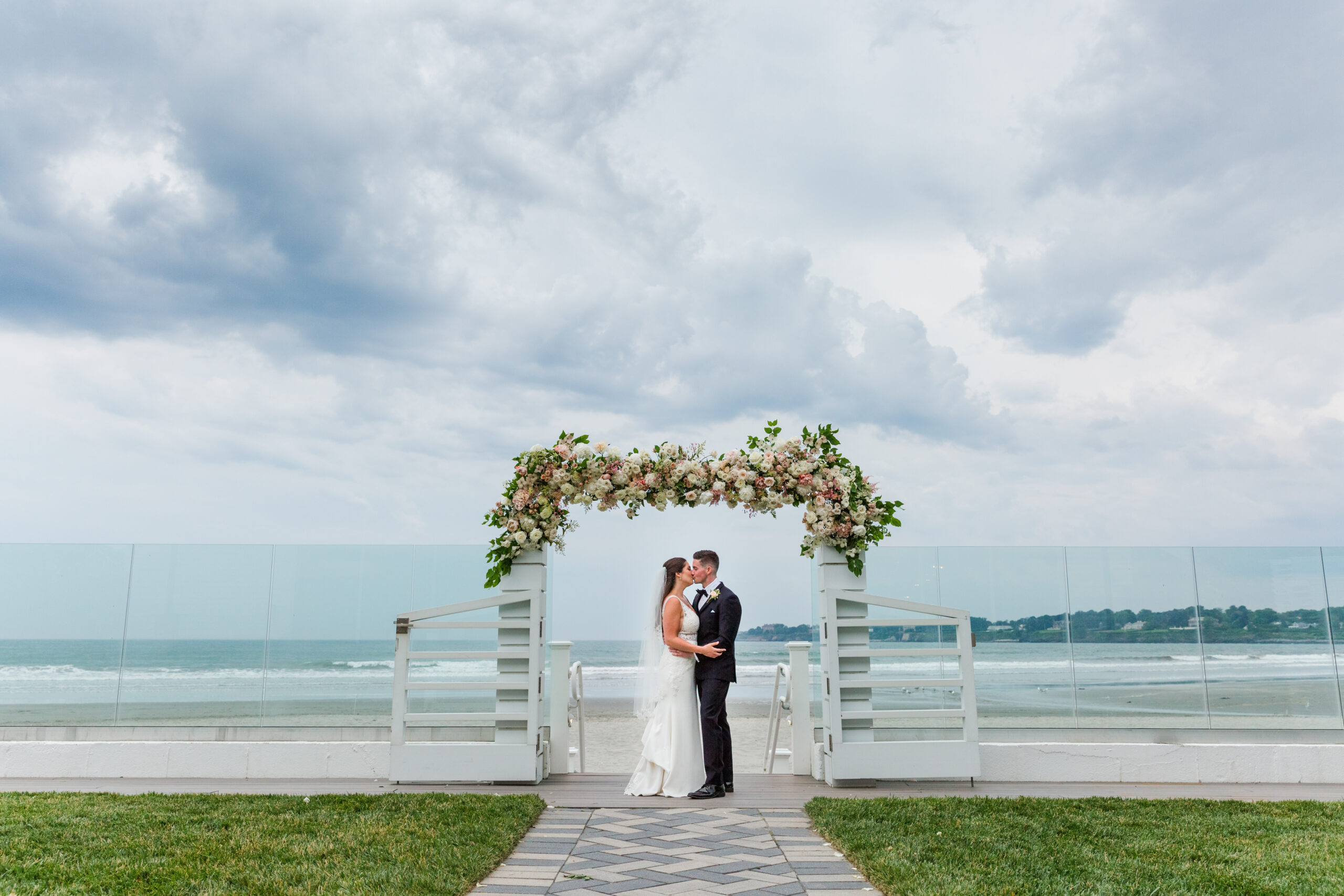 A bride and groom share a kiss under the flower arch on the porch of Newport Beach House 