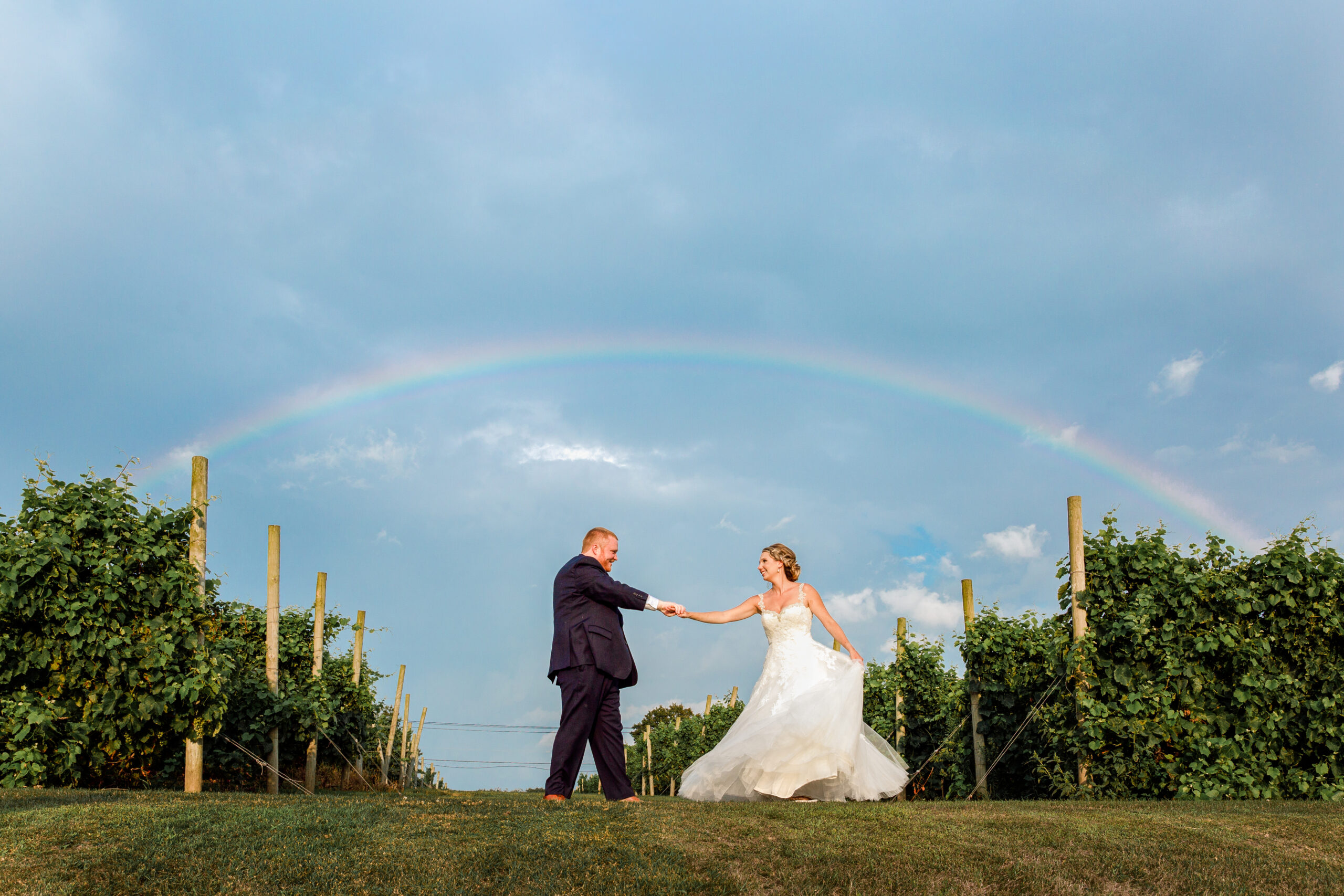 A bride and groom dance under an unexpected rainbow on their wedding day in the vineyards of Preston Ridge Vineyard. 