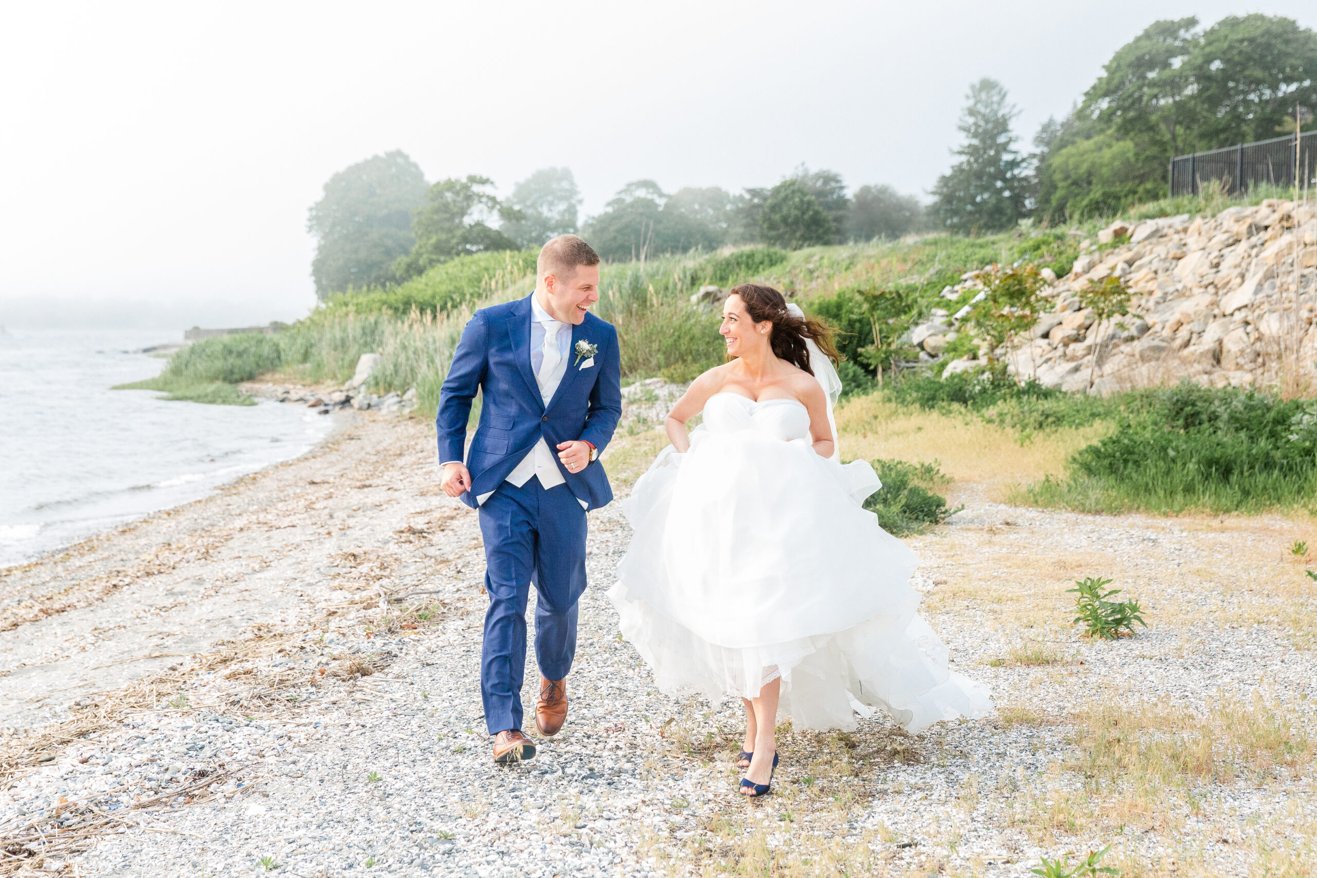 A bride and groom run on the beach of Warwick Country Club
