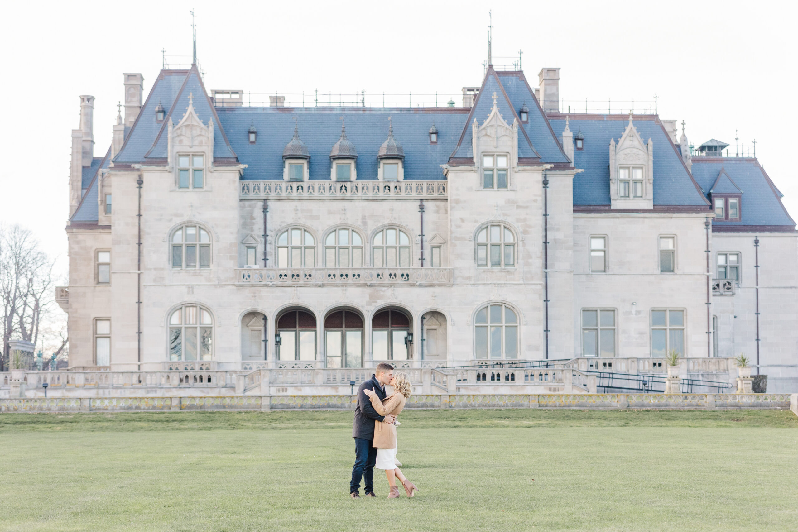 An engaged couple embrace on the back lawn of Ochre Court in Newport Rhode Island.